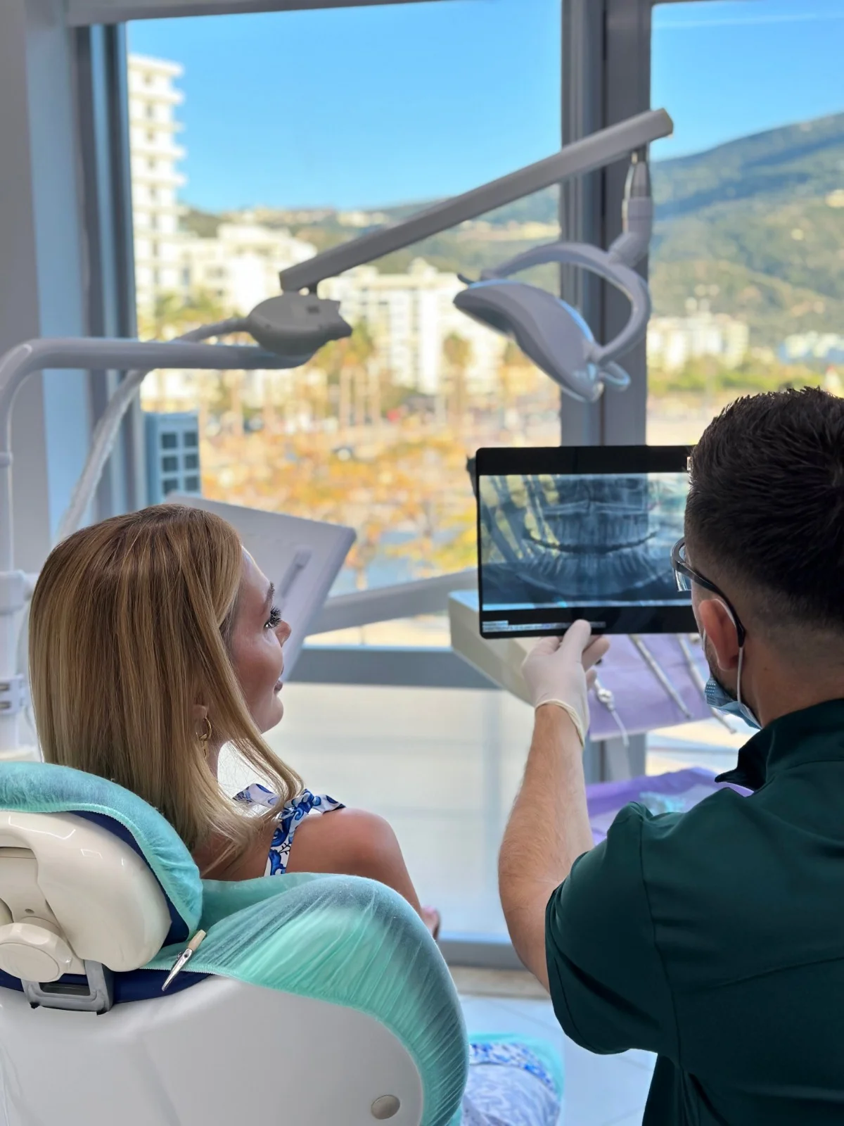 Doctor reviewing X-ray with patient at Valona Dental, Vlore coastline visible through the window